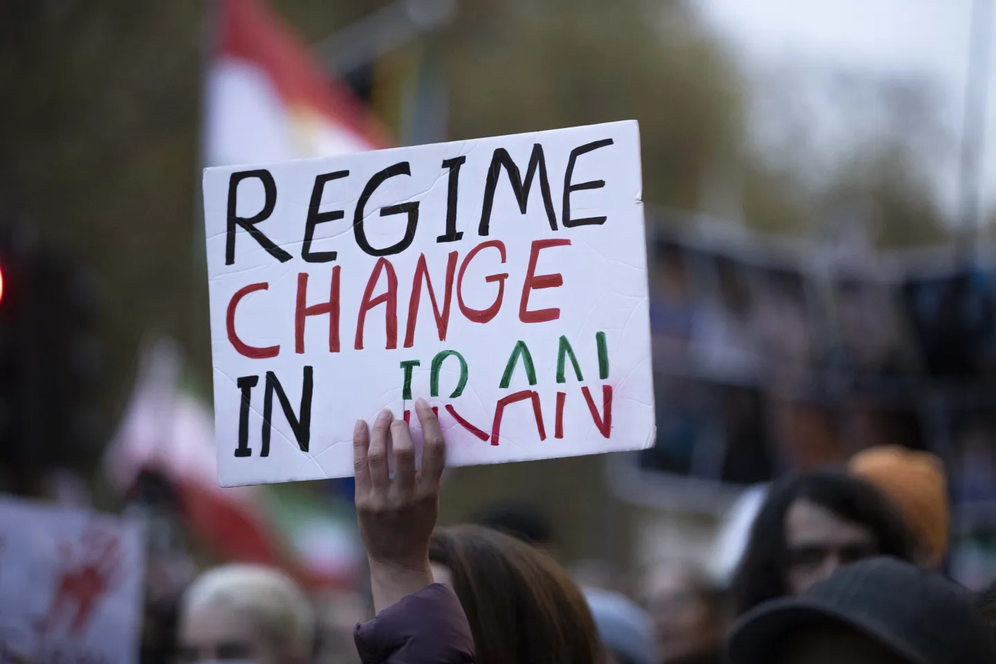 A protester holds aloft a hand-painted placard reading &lsquo;Regime Change in Iran&rsquo; in the colors of the Iranian flag.